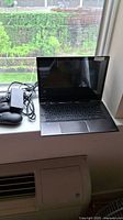 Toshiba laptop open on a windowsill with power adapter and three wireless mice beside it