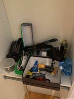 Shelf with a plastic container of nails, bolt cutter, ratchets, Allen key sets, caulk finishing set, other small tools and hardware supplies, and a blue cloth.