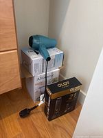 Teal hair dryer resting on boxes including Olov grooming kit box and Proactive humidifier box in corner
