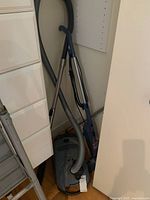 Miele canister vacuum and Bissell upright vacuum positioned side by side in a corner.