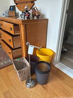 Wide view showing wooden dresser and floor with four waste bins and a chrome toilet paper holder standing