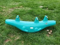 Photo of green plastic alligator-shaped teeter totter with three seating positions and hand grips, placed on grass.