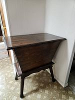 Wooden sewing box closed, showing dark wood stain, rectangular shape with angled sides and round legs.