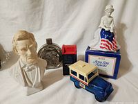 Photo showing Lincoln bust, Buffalo nickel flask, red and blue mail truck, white and blue mailbox, and Betty Ross figurine on original box