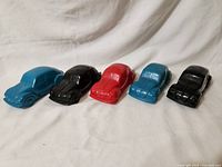 Photo showing full row of five Avon Volkswagen Beetle collectible bottles in various colors on fabric background.