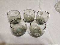 Front view of 5 smoked glasses with white Baltimore Colts and NFL logos, arranged on a white linen surface.
