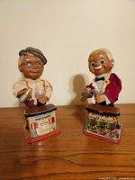 Pair of vintage tin bartender toys, one labeled Charlie Weaver Bartender, both holding cocktail shakers and glasses, standing on colorful bases.