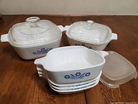 2 medium square white ceramic casserole dishes with Blue Cornflower pattern and glass lids, 4 mini white dishes stacked, and a plastic lid for mini dishes