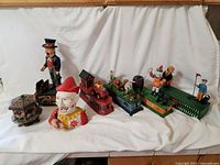 Seven cast iron mechanical banks lined up, including Uncle Sam, carousel with horses, and others in colorful painting.