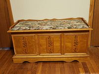 Front view of cedar chest showing floral inlaid panels and padded floral seat upholstery.
