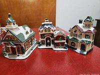 Photo of three ceramic light-up houses featuring a bell tower, red and green details, and multi-story structure