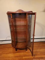 Front view of open curio cabinet showing interior shelves, wood frame, and curved glass door.