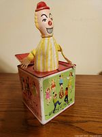 Front view of the Jack in the Box toy showing the clown figure popping out and illustrated panels on box sides.