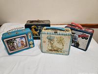 Front view of all four vintage metal lunchboxes together on a white cloth background.