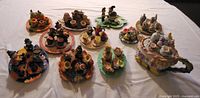 Overview of all twelve miniature holiday-themed mini tea sets arranged on a white tablecloth.