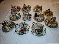Photo showing front and top view of 11 miniature nursery-themed tea set figurines on a white background, details of figurines, tea sets, and bases clear.