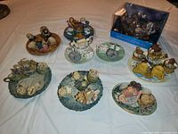 Photo shows ten miniature Noah's Ark themed miniature tea sets arranged on a white surface, featuring animals and small teacups or teapots on decorative bases.