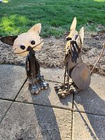 Two metal outdoor cat sculptures placed on a concrete patio with grass background, showing front and side views highlighting material and design details.