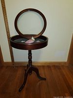 Full view of round wood pedestal table with hinged lift-top opened showing felt lining inside.