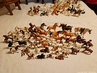 Overall view of various porcelain and ceramic animal figurines arranged on a sheet, including multiple horse figurines in different colors and breeds, as well as other animal figurines like dogs, cows, and pandas.