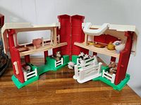 Fisher-Price Red Barn and Silo playset open with farm animal figures inside and around it, showing barn structure and animals.