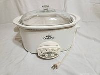 Full view of Rival Crock-Pot with glass lid and front control panel, white body, shows some signs of light use.