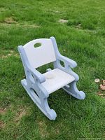 Front and side view of Little Tikes kids rocking chair placed on grass, showing light blue frame and white seat and backrest, with cut-out handle in backrest.