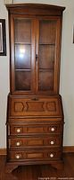 Front view of the secretary desk showing glass doors and drop front closed with drawers below.