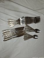 Photo shows an assortment of silverware including forks, knives, and spoons with swirled ornate designs on the handles.