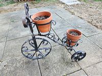 Tricycle planter with two terracotta pots placed on outdoor stone patio with grass in background.