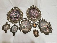 Eight assorted metal-framed vintage-style wall decorations with floral prints laid out on a white surface. Variety of sizes and shapes with visible wear.