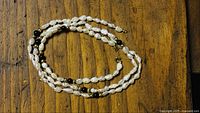 Freshwater pearl necklace and bracelet viewed coiled on wood surface, highlighting pearls and gold/black beads.