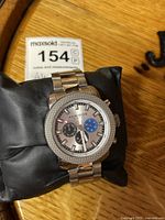 Front view of Akribos wristwatch showing gray dial, multi-tone subdials, and stainless steel bracelet on black pillow.