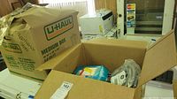 Four boxes on top of a white appliance, U-Haul medium box labeled with appliance cords note, assorted cords visible inside open boxes