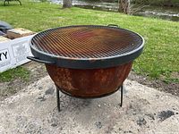 Front view of entire fire pit showing round cast iron bowl, three legs and grill grate on top