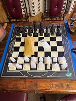 Full view of chess board with black and white stone-like chess pieces arranged with game ticket and envelope on board.