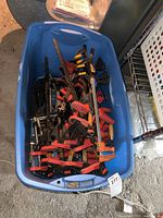 Blue plastic storage bin filled with a mixed assortment of clamps showing red, black, and some yellow clamps inside.