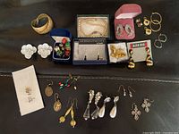 Overview of assorted custom costume jewelry focusing on various earrings and a pearl necklace on a dark leather surface.