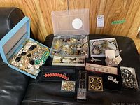 Full overview of assorted costume jewelry including bracelets, necklaces, brooches, earrings, and pens displayed on a sofa