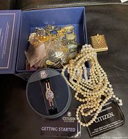 Overview photo showing assorted costume jewelry pieces in blue box and spread out, including bracelets, pins, faux pearls, earrings, and women's Citizen Eco-Drive wristwatch with box and instruction booklets.