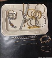 Wide shot showing multiple bracelets, bangles, chains on a tray and flat surface