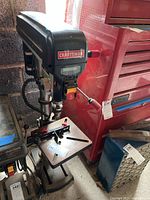 Front perspective showing the Craftsman brand name and the drill press with its adjustable table and laser guide attachment.