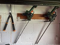Two Black and Decker electric hedge trimmers mounted on wall alongside Fiskars manual hedge trimmers.
