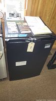 Front view of the black upright freezer with documents on top.