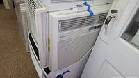 Front and side view of the white Frigidaire window air conditioner installed in a window with remote taped on top.