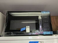 Front view of black over-the-range microwave with protective plastic and scratch wear