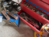 Cast iron anvil on blue stand next to wedges and open drawer showing pipe wrench