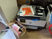 HP OfficeJet Pro 9010e series printer with related packing materials and several ink cartridges on and beside it.