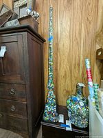 Photo showing the tall glass jar filled with marbles next to wooden furniture, emphasizing the height and shape of the jar.