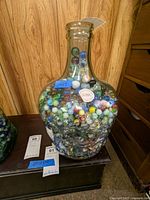 Full view of large, heavy, clear glass jar with embossed details, filled with a variety of colorful glass marbles, showing jar shape and content quantity.